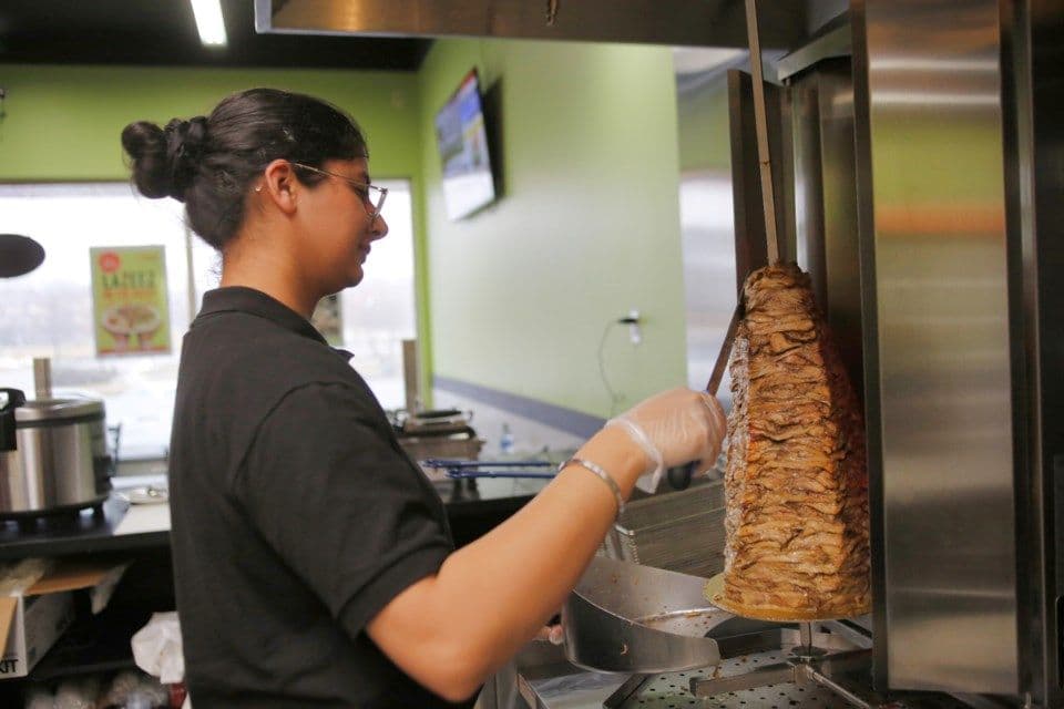 Women cutting chicken off spit at lazeez location